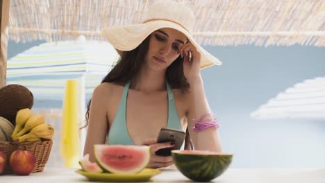 Schöne-junge-Frau-im-Chat-mit-ihrem-Handy-am-Strand