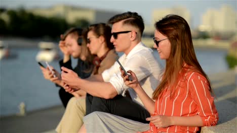 Vier-Freunde-lachen-glücklich-und-beobachten-Social-Media-In-einem-Smartphone-in-der-Straße.-Jeder-mit-seinem-eigenen-Handy.-Beste-Freunde-und-Studenten-verbringen-Zeit-zusammen-im-Freien