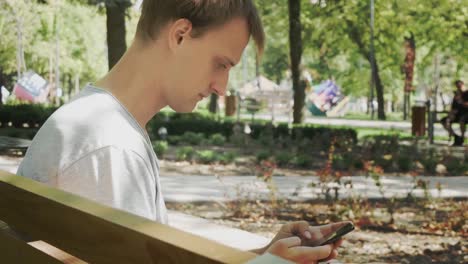 Hombre-chateando-en-el-teléfono-móvil.-Chico-relajado-sentarse-y-mirando-el-teléfono-móvil-en-City-Park.-Hermoso-macho-tener-chat-usando-Smartphone-al-aire-libre.-Hombre-charlando-con-un-amigo.