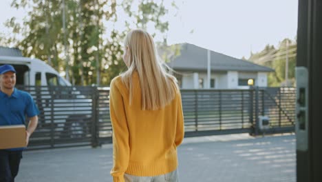 Schöne-junge-Frau-Holding-geliefert-Karton-Paket,-sie-unterzeichnet-elektronische-Signatur-POD-Gerät,-sagt-Abschied-von-Lieferung-Mann.-Paket-Lieferung-in-Vorort-Nachbarschaft.-Zeitlupe-Nzwinkel