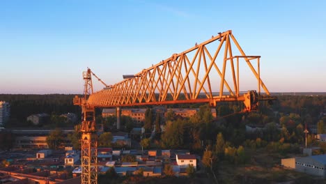 Una-grúa-de-construcción-balanceándose-ligeramente-en-el-viento-contra-el-cielo-de-la-mañana.-Primer-plano,-vídeo-aéreo