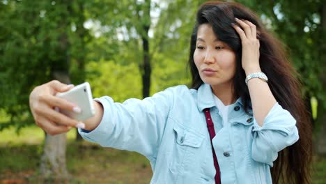 Hermosa-dama-asiática-tomando-selfie-al-aire-libre-en-el-parque-posando-el-dispositivo-de-retención-sonriente