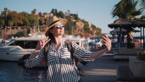 Millennial-hipster-mujer-turista-en-traje-casual-con-mochila-haciendo-selfie-en-muelle-de-yates,-puerto-deportivo