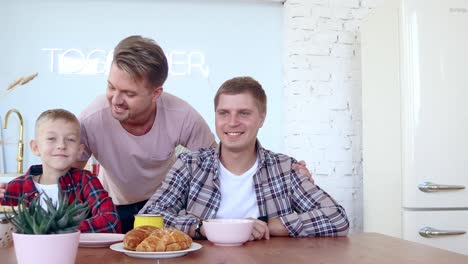 Glückliche-schwule-Familie-zwei-Väter-und-Sohn-frühstücken-in-der-Küche.