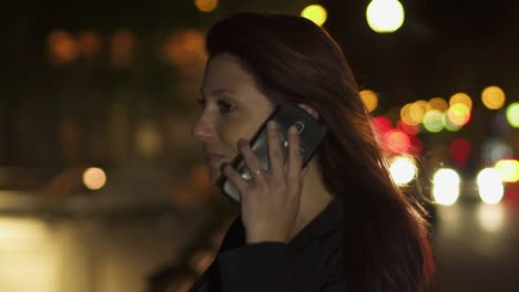 Happy-Attraktive-Rothaarige-Frau-mit-schwarzer-Jacke-und-roten-Haaren-mit-Telefongespräch-auf-ihrem-Smartphone-in-der-Nacht.-Paris-4K-UHD.-Zeitlupe.