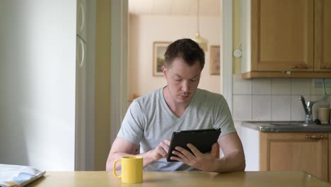 Junger-nachdenklicher-Mann-mit-digitalen-Tablet-sam-es-am-Fenster