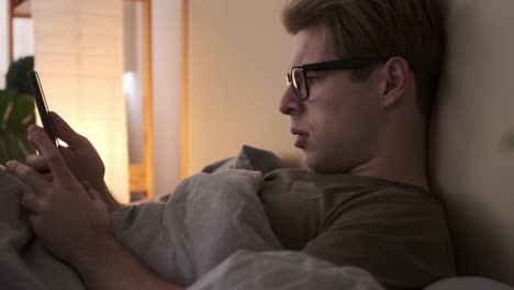 Young-man-using-mobile-phone-in-bed