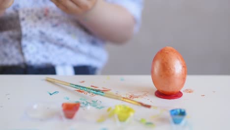 A-little-child-puts-an-orange-Easter-egg-on-a-stand.