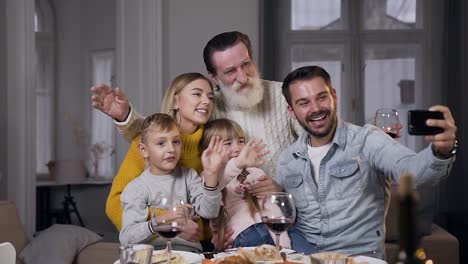 Frontansicht-der-charmanten-lachenden-Familie,-die-am-Esstisch-sitzt-und-Selfie-macht