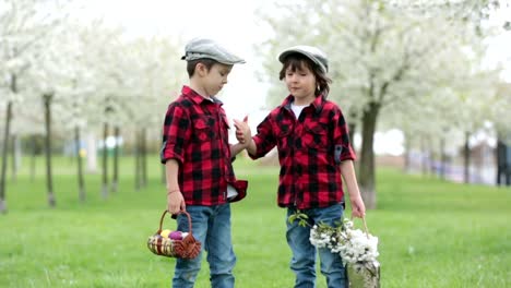 Dos-niños,-hermanos-niño,-divertirse-con-los-huevos-de-Pascua-en-el-parque,-jardín-floreciente-de-hermosa-primavera