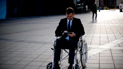 Disabled-Businessman-sitting-in-wheelchair-outdoor-and-work-with-tablet-PC