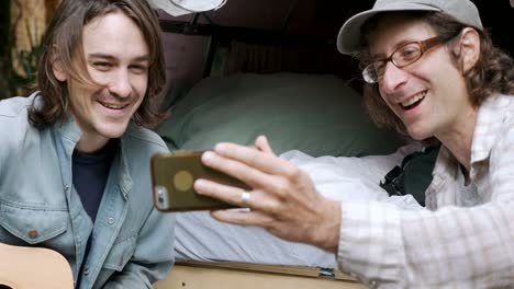 Two-handsome-men-talking-selfies-with-their-smart-phone-camping-together