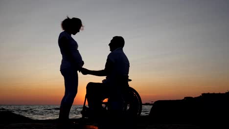 disabled-husband-in-wheelchair-holds-arm-wife-with-big-belly