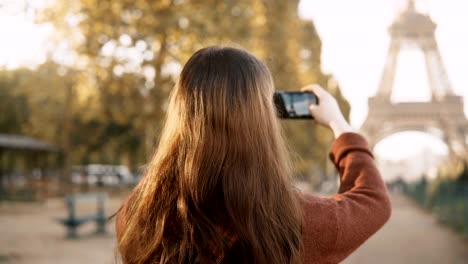 Back-view-of-young-woman-taking-photos-on-smartphone.-Teenager-tourist-exploring-the-Eiffel-tower-in-Paris,-France