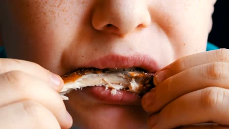 Close-up-view-of-teenager's-mouth.-A-boy-with-an-appetite-eats-a-fried-chicken-wing-in-a-fast-food-restaurant