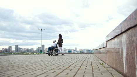 Hombre-discapacitado-en-silla-de-ruedas-con-mujer-joven-caminando-en-la-calle-de-la-ciudad