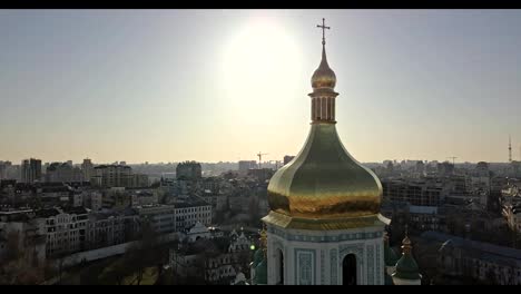 A-bird's-eye-view,-panoramic-video-from-the-drone-in-FullHD-to-the-golden-dome-of-the-bell-tower-of-Saint-Sophia's-Cathedral-in-the-city-of-Kiev,-Ukraine-against-a-bright-sun.