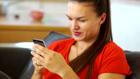 The-brunette-holds-a-mobile-phone,-writes-a-message-and-smiles.-Focus-on-a-mobile-phone-in-the-hands-of-a-girl