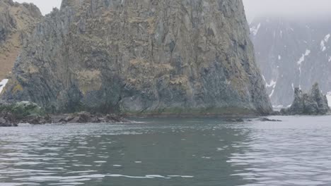 Isla-rocosa-y-montañas-nevadas-en-vista-panorámica-al-mar-desde-barco