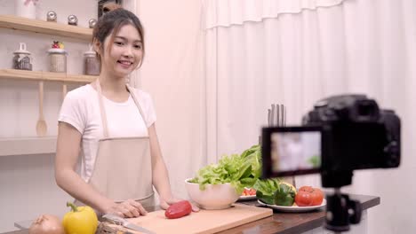 Mujer-asiática-blogger-usando-cámara-de-grabación-cómo-hacer-comida-sana-ensalada-video-para-su-abonado,-verduras-orgánicas-de-uso-femenino-preparar-ensalada-para-cuerpo-en-forma-en-casa.-Concepto-de-comida-sana.