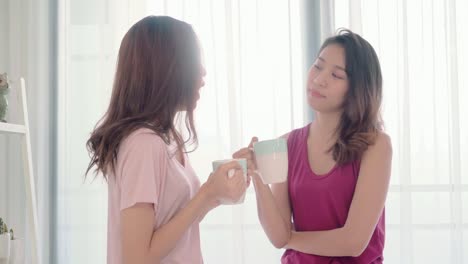 Young-Asian-women-lesbian-happy-couple-talking-and-drinking-coffee-in-bedroom-at-home,-enjoy-love-moment-while-lying-on-bed-when-relaxed-in-morning.-Lifestyle-LGBT-couple-together-indoors-concept.