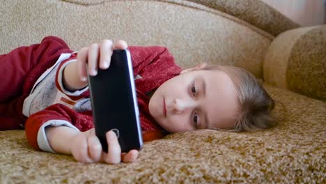 Girl-teenager-watching-a-video-in-the-phone-while-lying-on-the-couch.