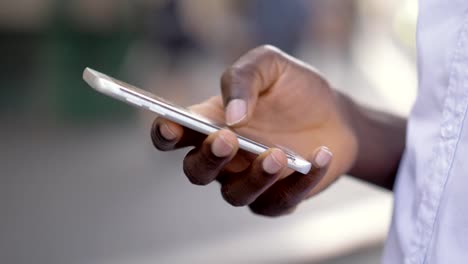 Nahaufnahmen-Porträt-des-jungen-afrikanischen-Man-es-Hands-Holding-Modern-Smartphone.-Schwarzer-Mann-tippen-am-Telefon-in-der-Innenstadt