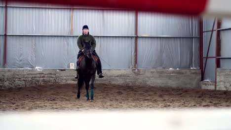 en-especial-hangar,-un-joven-con-discapacidad-aprende-a-montar-un-caballo-negro,-pura-sangre,-Hipoterapia.-el-hombre-tiene-una-prótesis-en-lugar-de-su-pierna-derecha.-concepto-de-rehabilitación-de-personas-con-discapacidad-con-los-animales