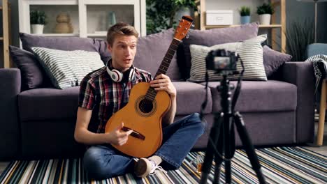 Young-blogger-is-recording-tutorial-about-playing-guitar-for-internet-blog-using-camera-at-home