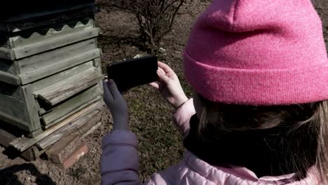 Chica-usando-el-teléfono-inteligente-cerca-de-abeja-colmena