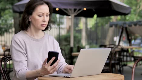 Anciana-usando-Smartphone-y-Portátil,-Sentado-en-Cafe-al-aire-libre