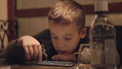 Niño-aburrido-usando-teléfono-inteligente-en-el-café