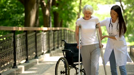 Doctor-helping-disabled-old-woman-walking-with-crutches,-recovery-after-trauma