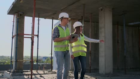 Supervisor-de-un-edificio-en-construcción-discutiendo-con-la-diseñadora-de-ingeniería-el-progreso-de-la-construcción-y-examina-un-plan-de-construcción