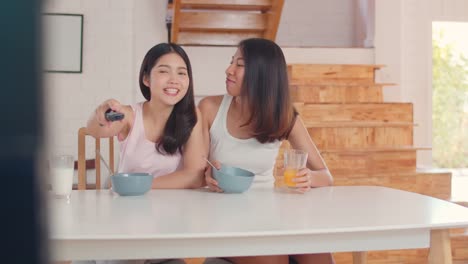 Asian-Lesbian-couple-watching-TV-while-have-breakfast-on-table-in-kitchen-in-morning-concept-at-home.