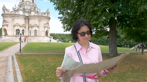 brunette-woman-looks-at-paper-map-against-the-background-of-a-historic-building