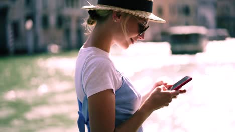 Positive-hipster-girl-dressed-in-summer-outfit-taking-pictures-of-Venice-showplaces-during-touristic-boat