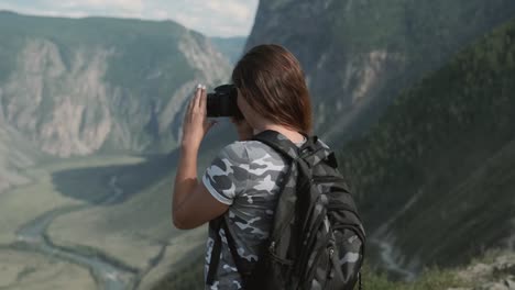 Weibliche-Reisende-macht-schöne-Bilder-mit-der-Kamera,-während-sie-auf-dem-Gipfel-des-Berges-steht.