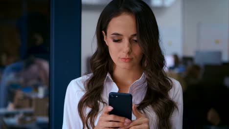 Retrato-de-hermosa-mujer-joven-usando-Smartphone-en-la-oficina.-Señora-de-negocios-con-camisa-blanca-escribiendo-mensajes-en-su-teléfono-móvil.