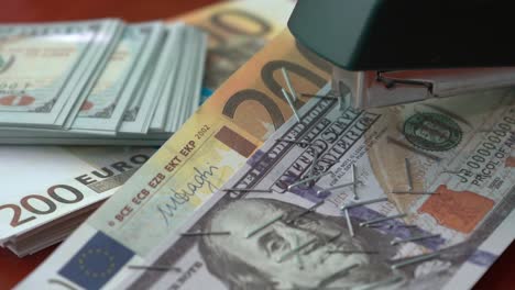 The-stapler-fastens-the-dollar-and-euro-notes-with-iron-clips.-Stapler-with-paper-clips-on-the-background-of-banknotes.-Counterfeit-money