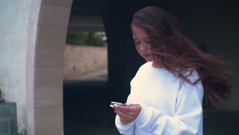 A-girl-stands-on-the-background-of-the-stone-arches-of-the-building,-holding-a-smartphone-in-her-hands.