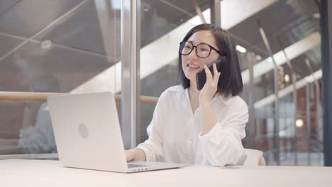 Hübsche-asiatische-Frau-mit-Telefonanruf-am-Arbeitsplatz