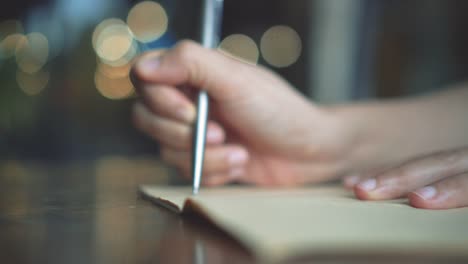 4K-Video-Kopie-Raum-des-Mannes-Hand-schreiben-in-weißen-Notizbuch-mit-Bokeh-Licht-im-Café-Hintergrund.