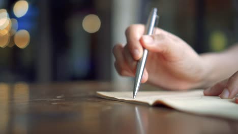 4K-video-copy-space-of-man-hand-writing-down-in-white-notebook-with-bokeh-light-in-cafe-background.