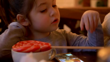 pequeño-niño-ve-vídeo-en-el-teléfono-inteligente-en-la-mesa-en-el-café