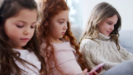 Gruppe-von-Mädchen-mit-Freunden-sitzen-auf-dem-Sofa-zu-Hause-spielen-auf-digitalen-Tablet-und-Handys