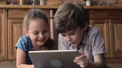 Little-siblings-lying-on-floor-having-fun-using-tablet