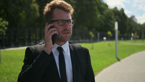 Businessman-talking-on-smartphone-outdoors,-electric-scooter-nearby