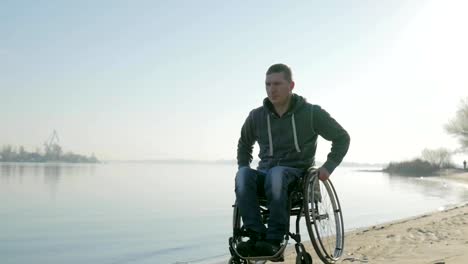 Disabled-man-goes-to-embankment-along-sea-in-wheelchair,-portrait