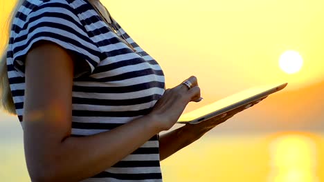 Close-up-a-girl-uses-a-tablet-by-the-sea-on-the-sunset.